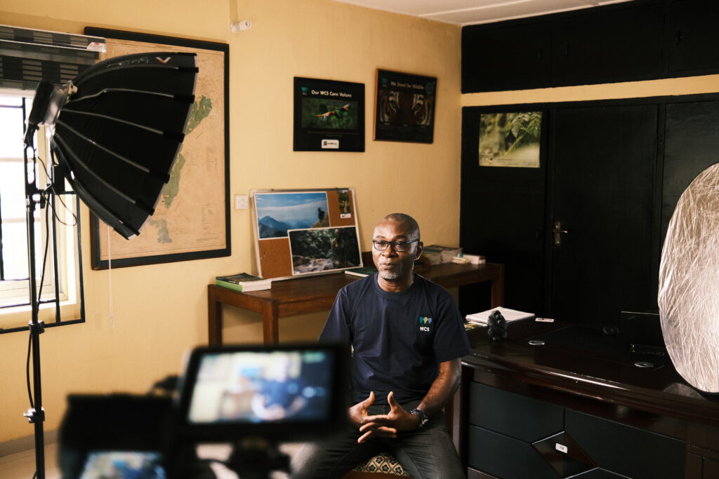 WCS staff member being filmed for an interview, with lighting and camera equipment in an office