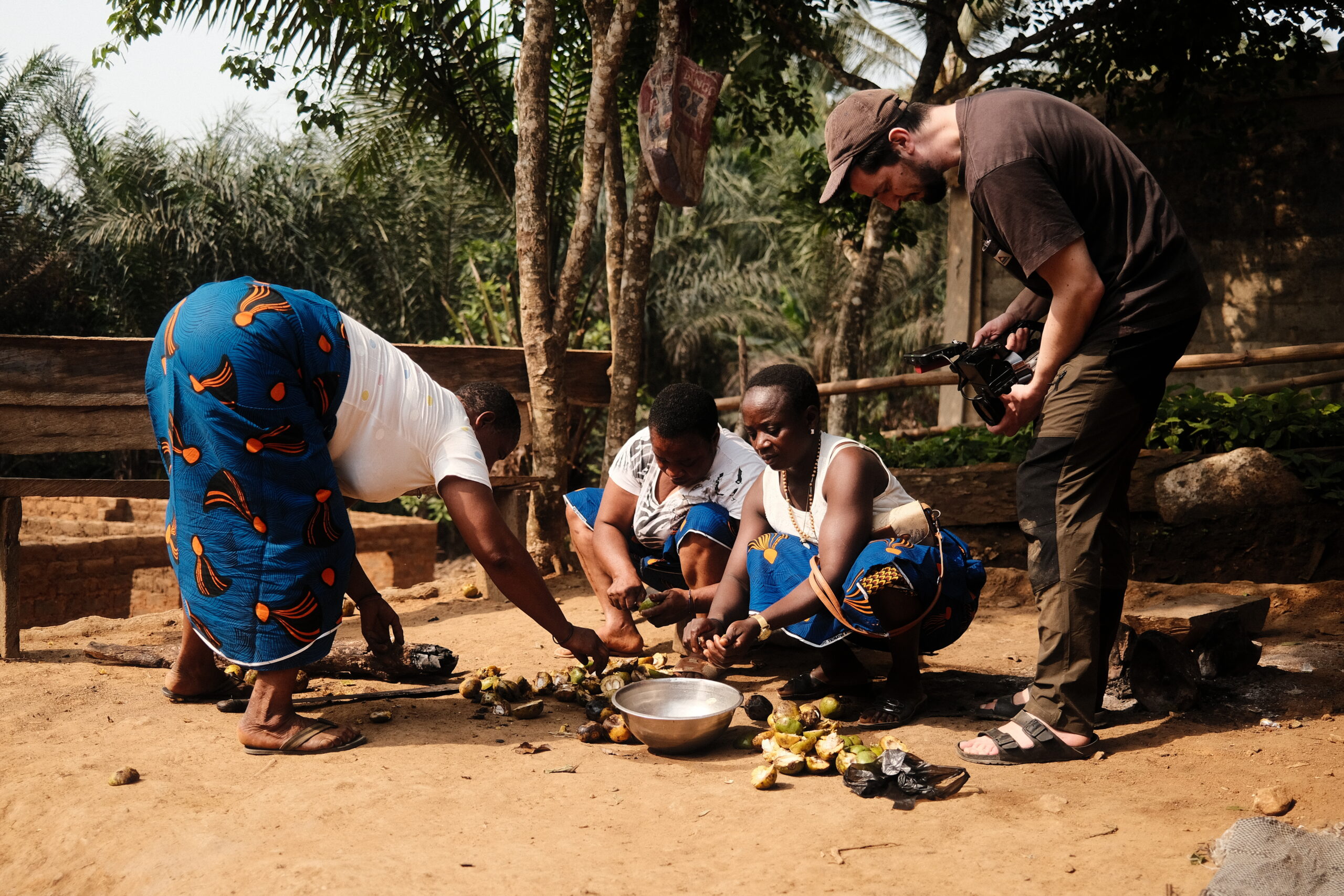 Cameraman filming local women preparing bush mango seeds together in a village setting
