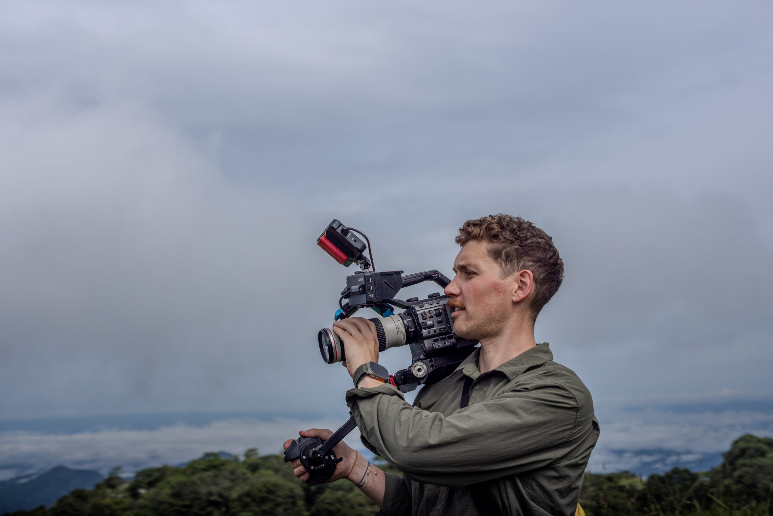 Cinematographer filming with a cinema camera overlooking misty forested hills at Gashaka Gumti